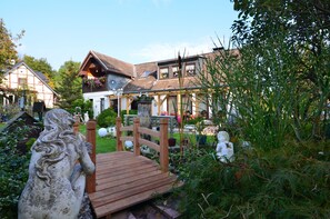 A traditional European house with a wooden bridge leading to the entrance, surrounded by lush greenery and statues. - Gemutliches Ferienhaus mit Pool in Blankenburg (Blankenburg)