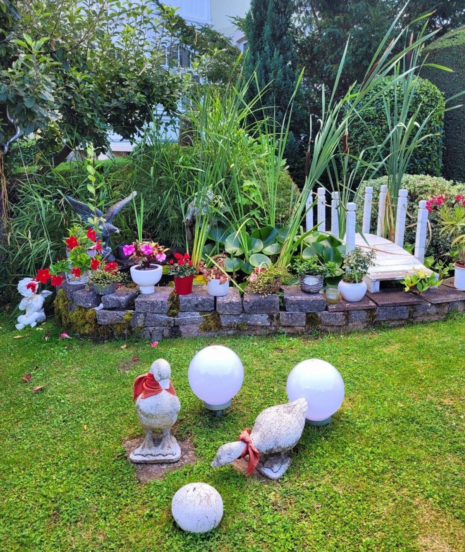Un jardín con diversas plantas, una cerca blanca y estatuas decorativas de pájaros.