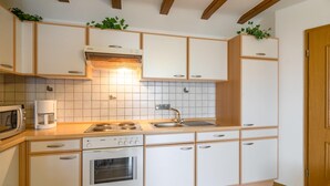 A modern kitchen with white cabinets, a built-in oven, a microwave, a coffee maker, and a sink. - Eschfeld Sauna Apartment (Eschfeld)