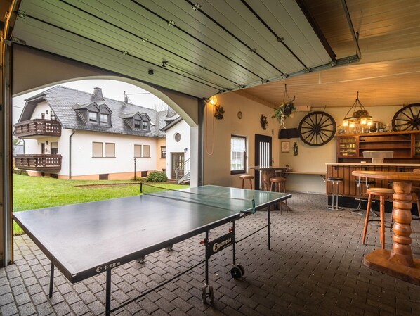 An indoor ping pong table with a view of a house through an archway.