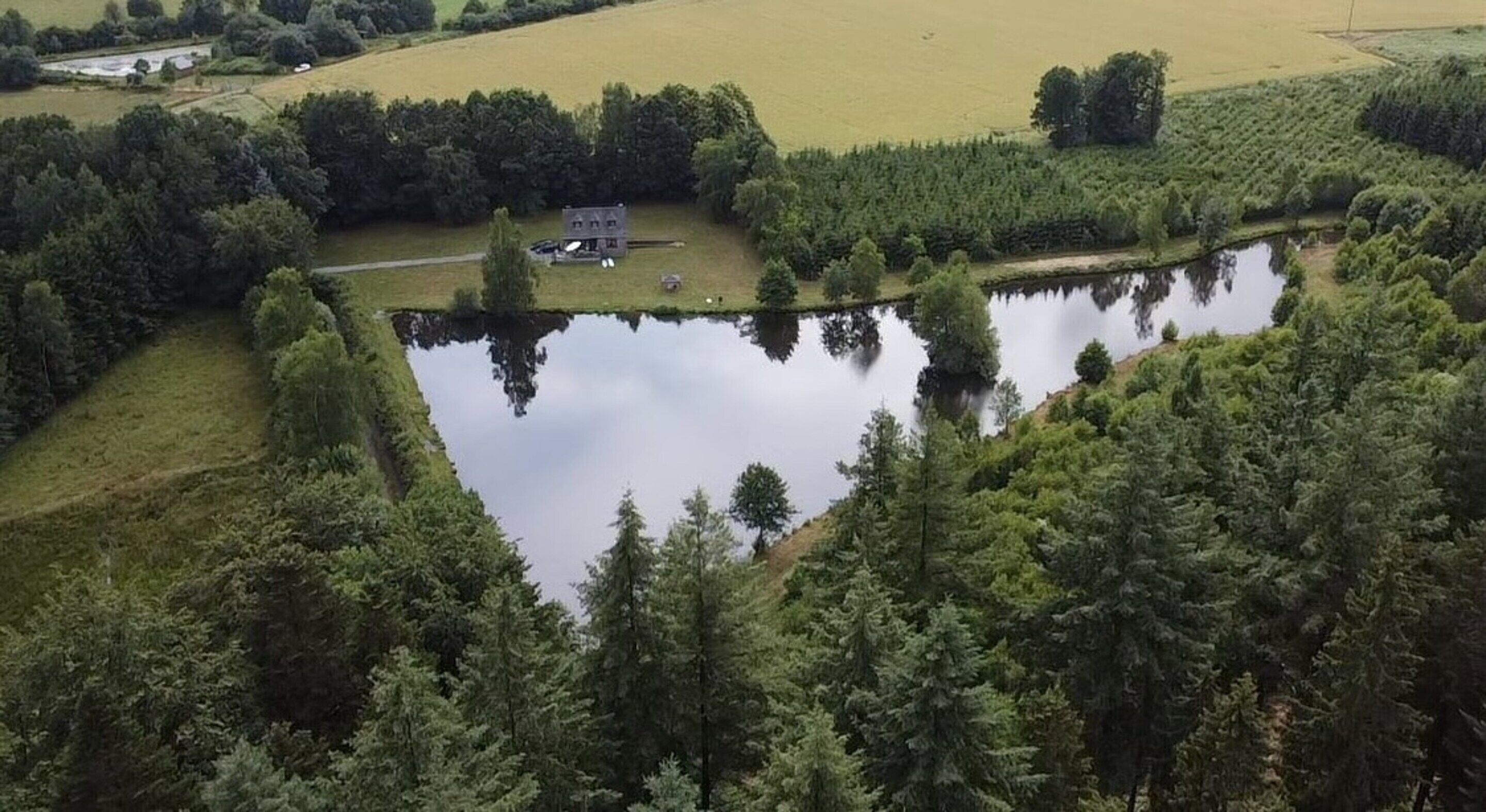 Une vue aérienne d’un lac entouré d’une forêt dense, avec un petit bâtiment situé près du bord de l’eau.