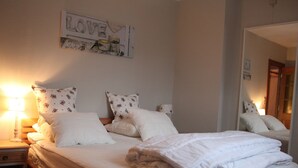A neatly made bed with white linens and floral-patterned pillows, a bedside lamp, and a wall-mounted sign that reads "LOVE". - Lakeside Getaway in Bouillon (Paliseul)
