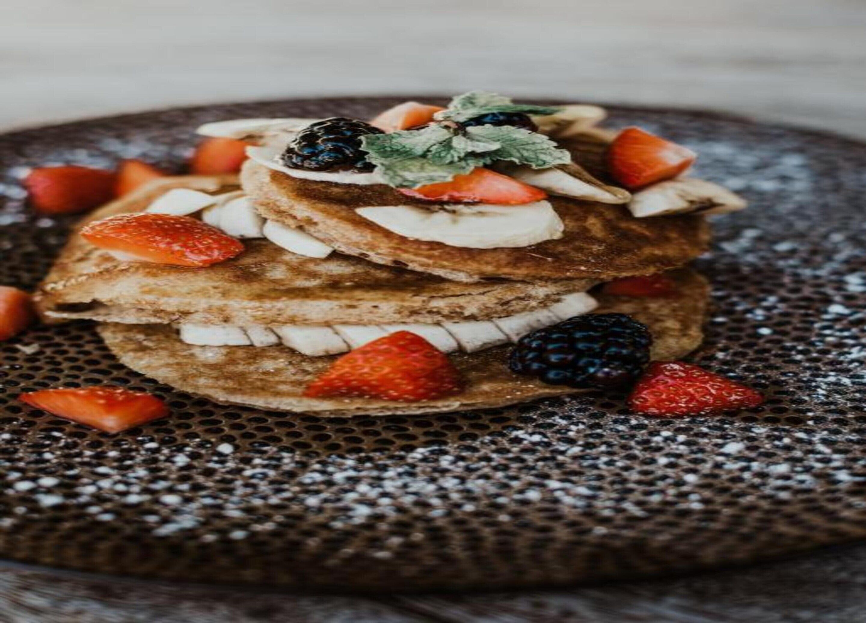 Ein Stapel Pfannkuchen mit Erdbeeren und Brombeeren auf einer strukturierten Platte.
