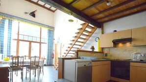 A kitchen with wooden cabinets, a dishwasher, and a dining area with chairs and a table. - Vintage Home With Pets (Daverdisse)