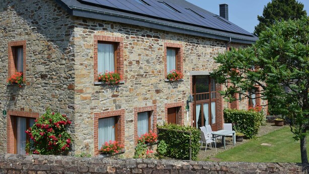 A stone building with multiple windows, a solar panel roof, and a small outdoor seating area. - Vintage Home With Pets (Daverdisse)