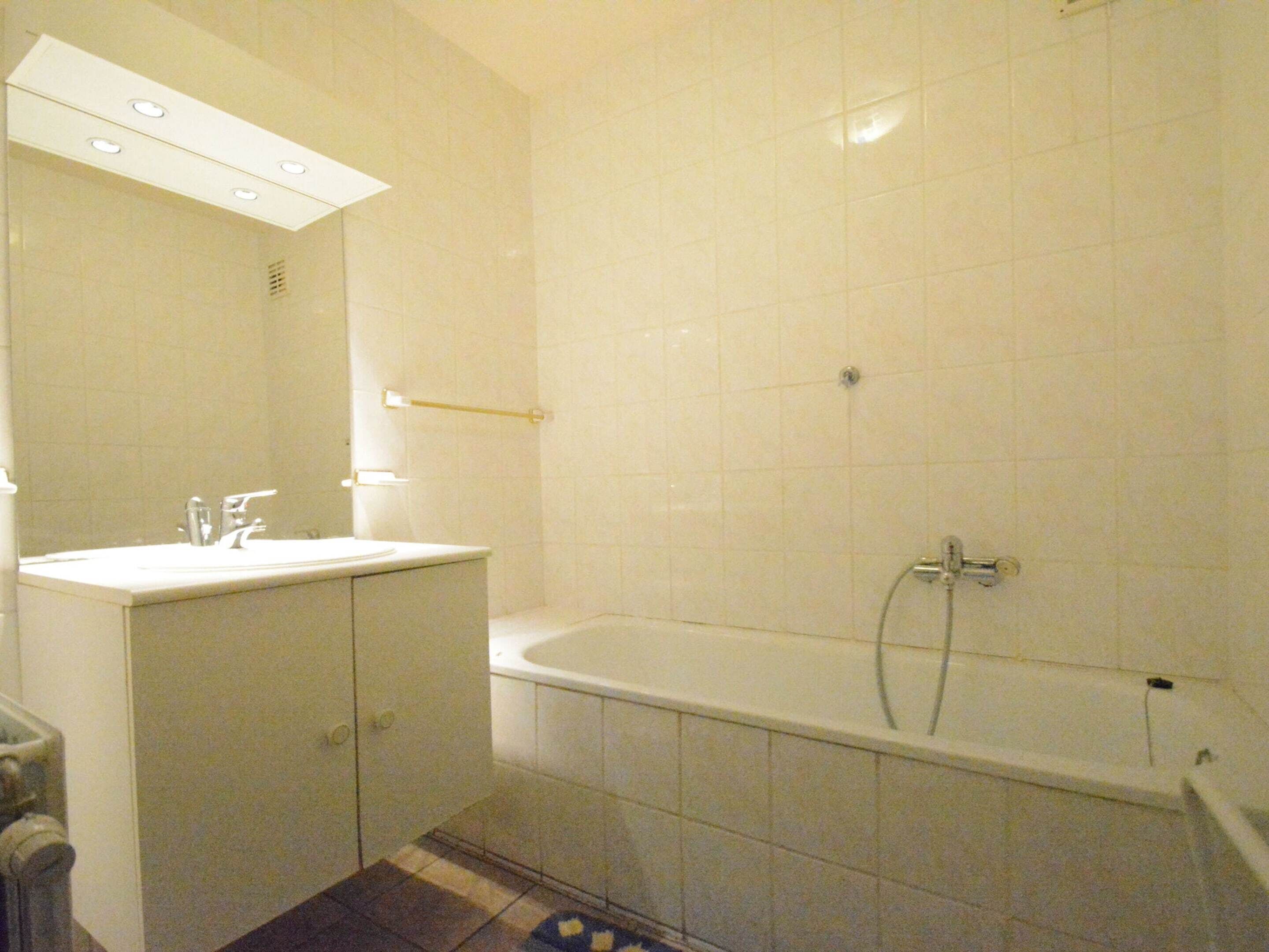 Une salle de bain avec un lavabo blanc, un miroir et une baignoire.
