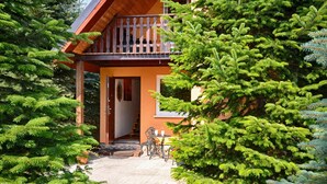 Une cabane en bois dotée d’un balcon, entourée d’une forêt dense de conifères.