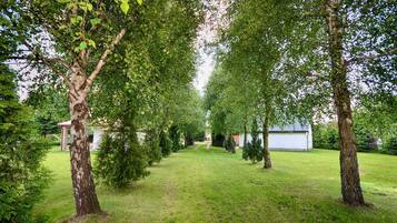 A well-maintained garden with a variety of trees and shrubs, a clear pathway, and a small building in the background.