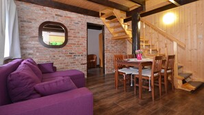 Une pièce chaleureuse avec un canapé violet, une table à manger en bois et des chaises. On peut voir un mur en briques et des poutres en bois.