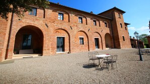 A historic brick building with arched doorways and windows, a gravel courtyard, and outdoor seating. - Belvilla by OYO Fiore (Montepulciano)
