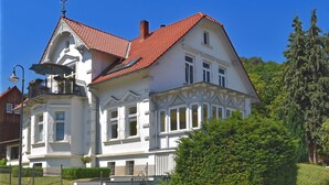 Un grand bâtiment blanc, doté d’un toit recouvert de tuiles rouges, de nombreuses fenêtres et d’un balcon avec un lampadaire.