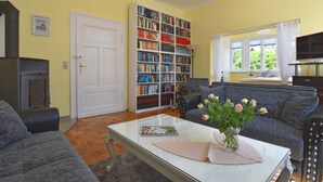 Un salon avec un canapé, une table basse sur laquelle se trouvent un livre et des fleurs, une bibliothèque, une cheminée et un téléviseur.