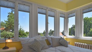 Une chambre dotée d’un grand lit, de nombreuses fenêtres et offrant une vue sur la verdure environnante.
