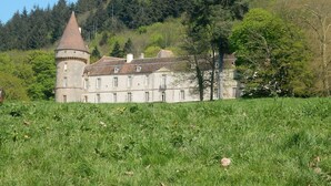 Ein historisches Gebäude mit einem Turm, umgeben von üppiger Vegetation und einem bewaldeten Hang.