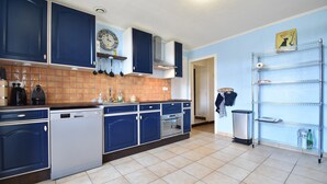 Eine Küche mit blauen Schränken, einem Geschirrspüler, einem Backofen und einem Metallregal.