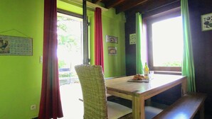 A room with a wooden table, wicker chair, and bench. There are curtains, a calendar, and a bottle on the table. - Spacious Country Villa (Neufchateau)