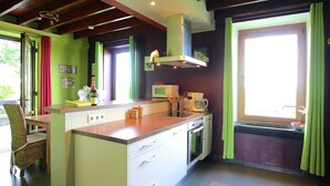 A kitchen with a central island, a microwave, and a coffee maker. There is a window with green curtains and a view of greenery outside. - Spacious Country Villa (Neufchateau)