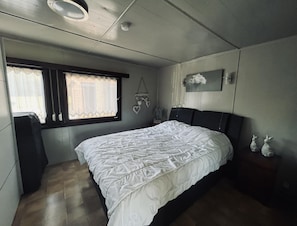 A bedroom with a bed, a window with curtains, a wall-mounted picture, and a ceiling light.