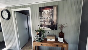 A wooden console table with a clock, a framed picture, and a vase with dried plants. - Modern Waterfront Chalet (Geel)