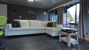 A modern living room with a sectional sofa, a wooden coffee table, and a view of the outdoors through large windows. - Modern Waterfront Chalet (Geel)