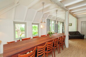 A dining area with a long wooden table and chairs, large windows, and a view of greenery outside. - Quaint Farmhouse in Waskemeer near Forest (Waskemeer)