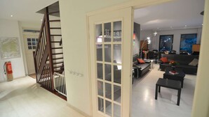 Een moderne woonkamer met een trap, een eetgedeelte en een uitzicht op de stad door grote ramen.