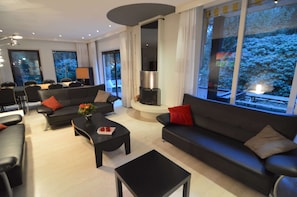A modern living room with a fireplace, a sofa, a coffee table, and a dining area. - Veluwe Edge Group Villa With Fire Pit (Doornspijk)