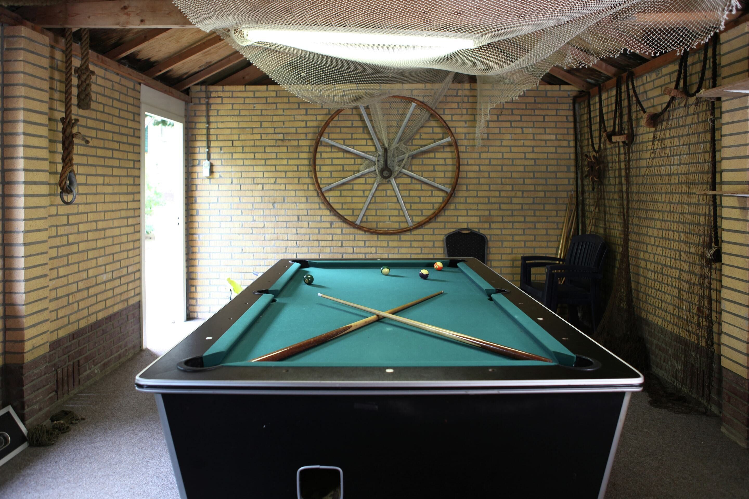 Een biljart met houten frame, een groot decoratief wiel en een net erboven.