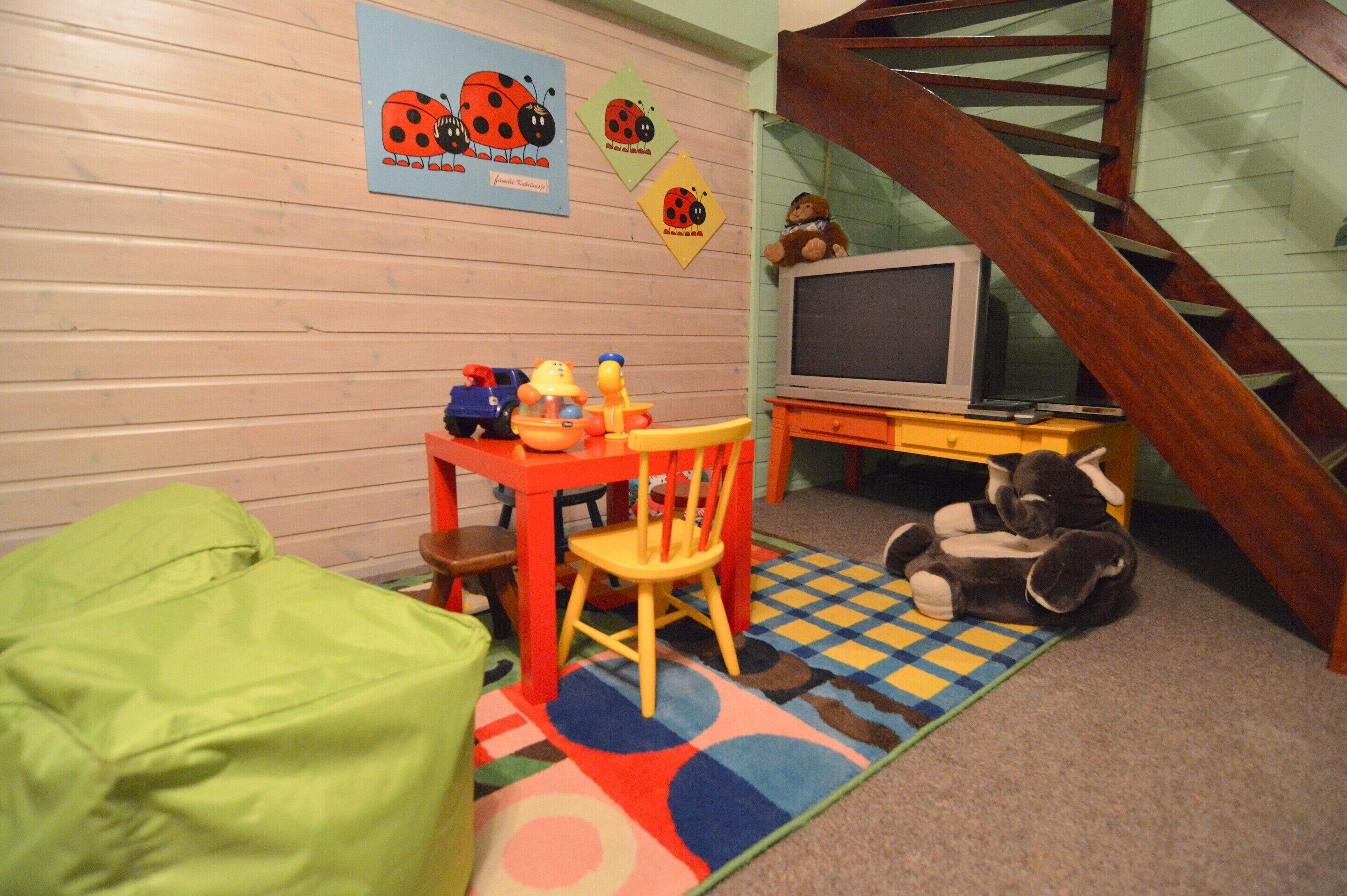 A children's playroom with wooden walls, a play table, chairs, a television, and a staircase.