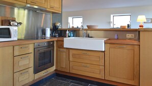 A modern kitchen with wooden cabinets, a stainless steel range hood, a built-in oven, a sink, and a window above the counter. - Holiday Home in Izier With Roofed Terrace, Garden, Parking (De Panne)
