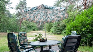 Ein Sitzbereich im Freien mit einem runden Tisch, Stühlen, einem Blumen-Sonnenschirm und einem Tisch mit dekorativen Gegenständen.