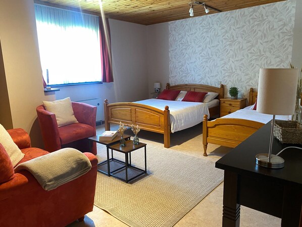 Ein Hotelzimmer mit einem hölzernen Bett, einem roten Sessel, einem kleinen Tisch mit einem Buch und einer Nachttischlampe.