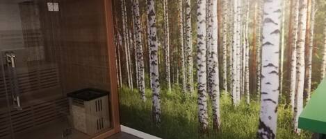 A bathroom with a glass shower enclosure, a green towel, and a wall mural of birch trees.