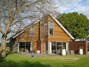 Een modern huis met grote ramen, een bakstenen schoorsteen en een verzorgd gazon.