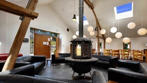 Un intérieur chaleureux avec un poêle à bois central, des sièges en cuir et une vue sur l’extérieur grâce à une grande fenêtre.