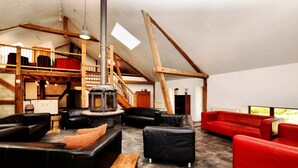 Un loft spacieux avec de hauts plafonds, des poutres apparentes, une cheminée et un mélange de canapés en cuir noir et rouge.