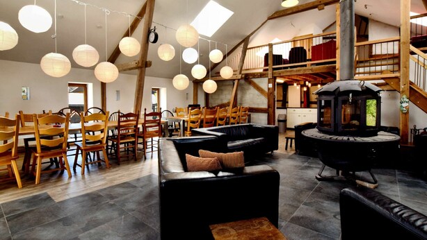 Un intérieur spacieux avec de hauts plafonds, des poutres en bois et un espace salon central agrémenté d’une cheminée.