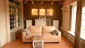A living room with a beige sofa, a small table, and artwork on the wall. - Holiday Home in Zele Near Laarne Castle (Zele)