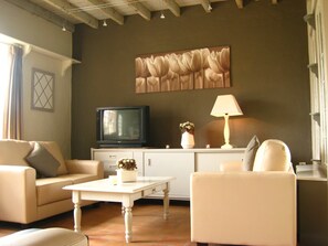 A living room with a television, a lamp, a vase with flowers, and a painting on the wall.