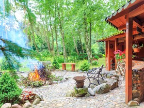 Un patio rústico al aire libre con una chimenea, asientos y una estructura de madera con plantas colgantes.