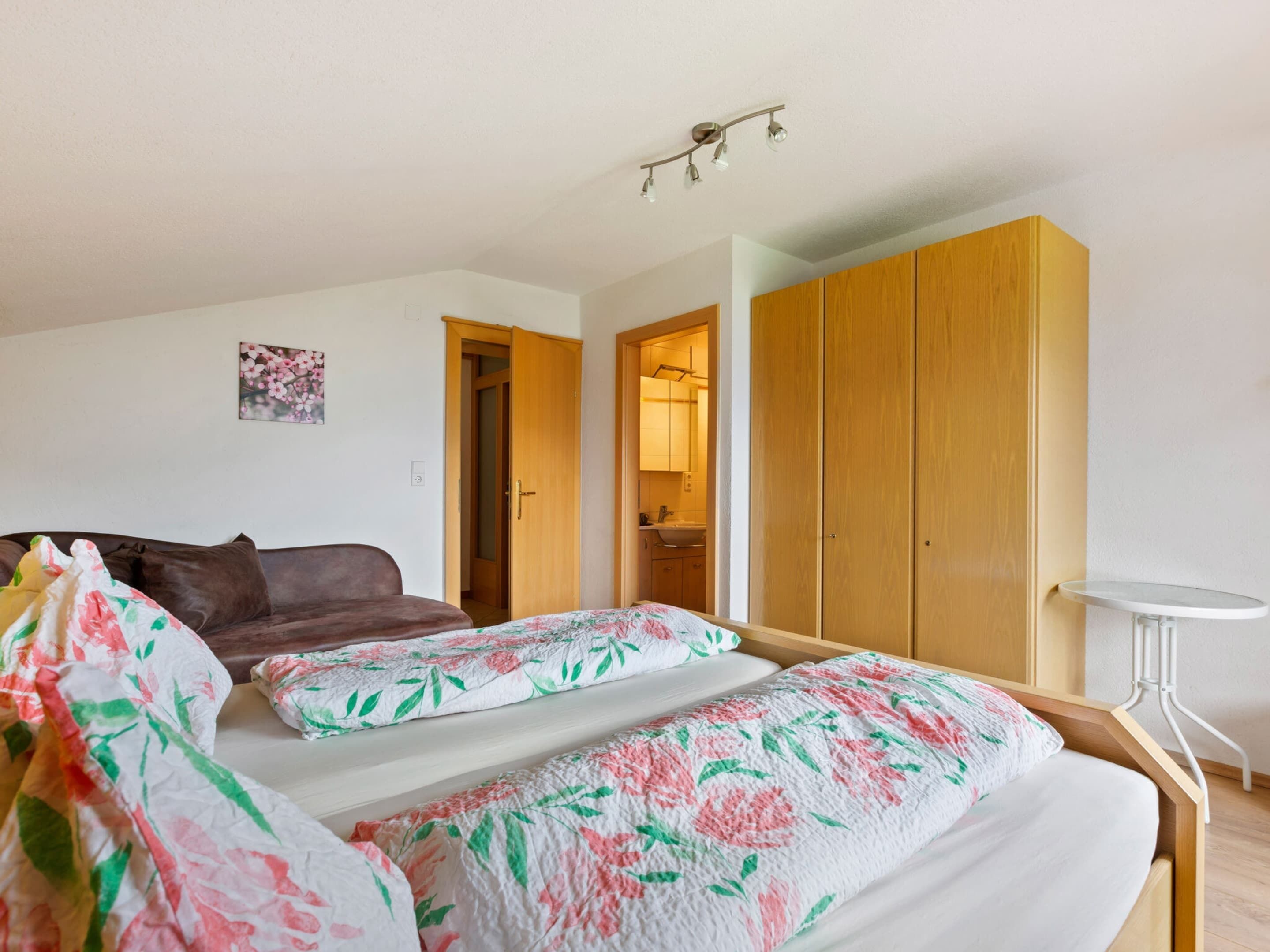 A bedroom with a bed, a wooden wardrobe, a small table, and a bathroom visible through an open door.