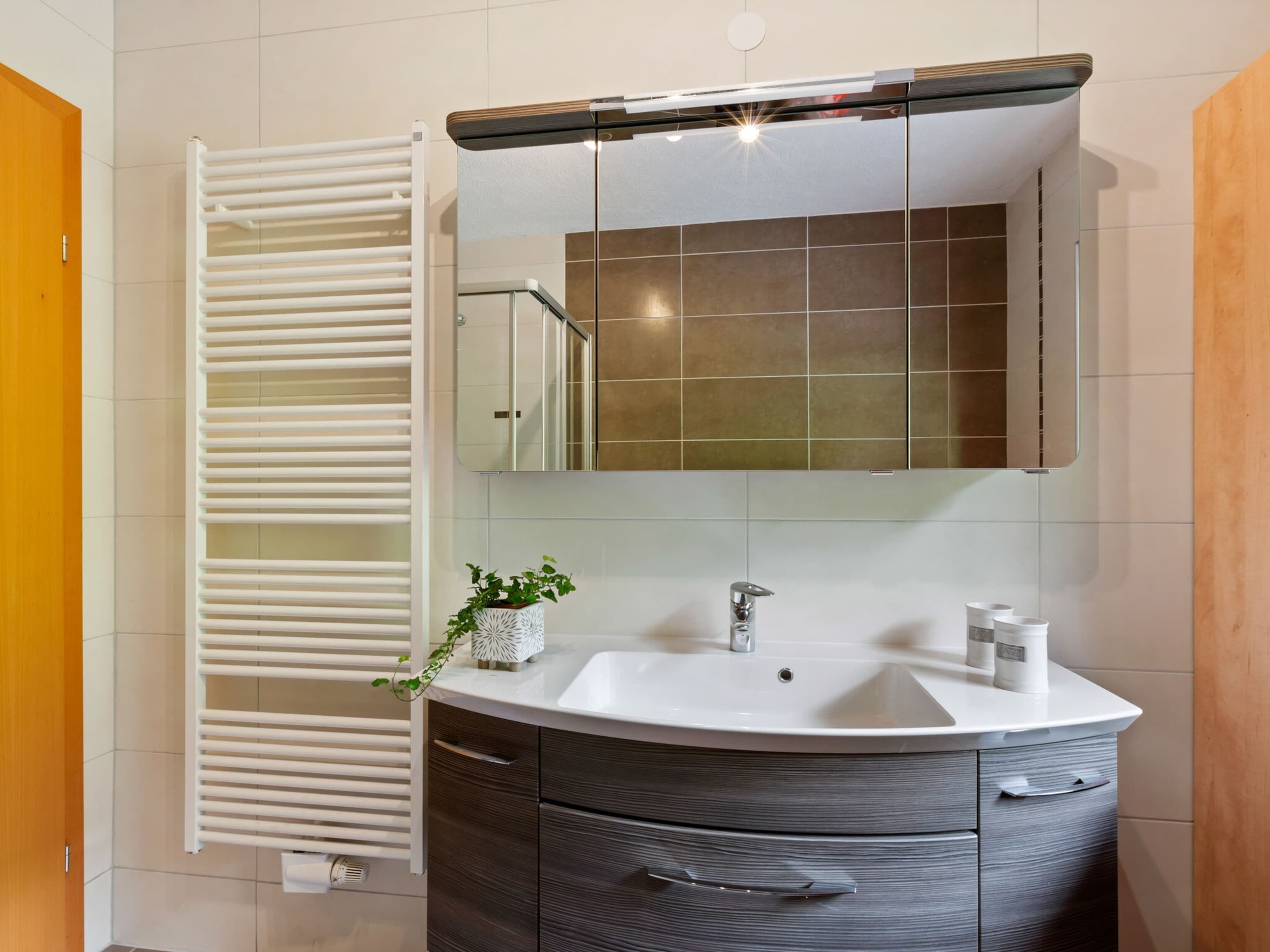 Un baño con lavamanos blanco, muebles de madera oscura, un espejo y un perchero blanco.