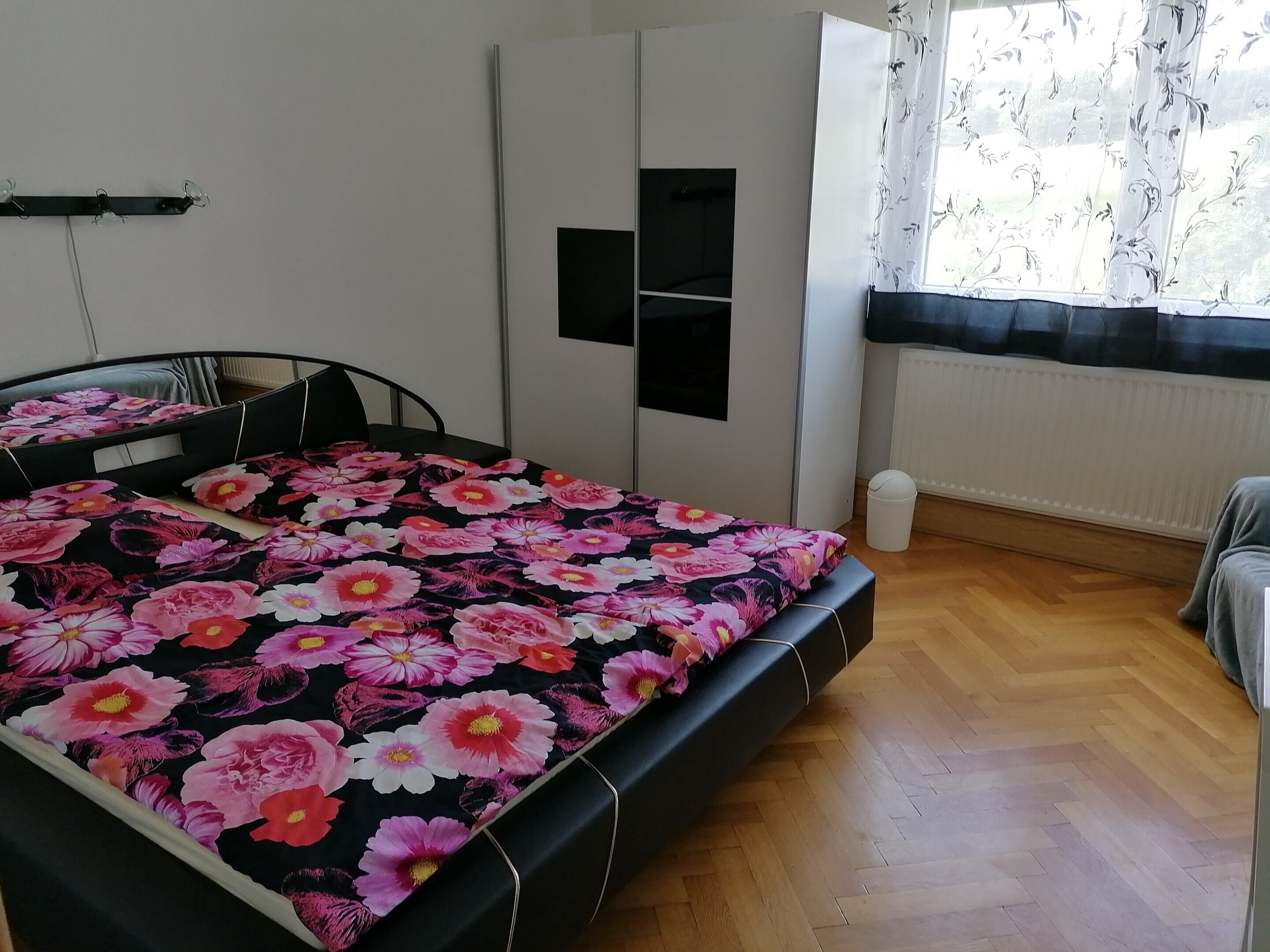 A bedroom with a bed, a wardrobe, a radiator, and a window with curtains.