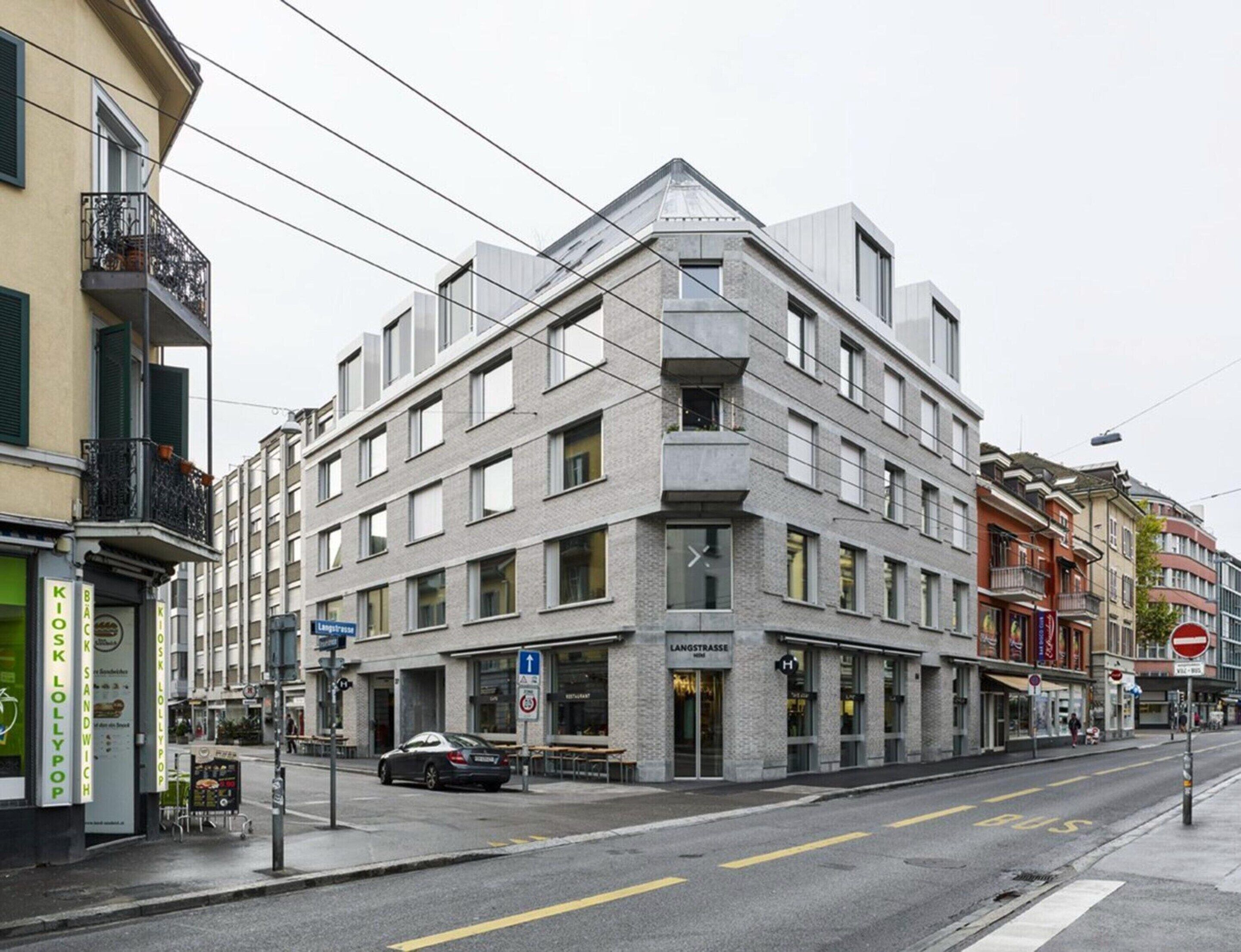 Un edificio de varios pisos con un diseño arquitectónico moderno, que presenta una entrada en esquina destacada y un letrero de restaurante visible.