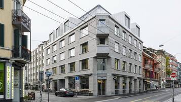Un edificio de varios pisos con un diseño arquitectónico moderno, que presenta una entrada en esquina destacada y un letrero de restaurante visible.