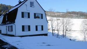 Et hvidt hus med to etager, skråt tag, mange vinduer og en parabolantenne på taget.