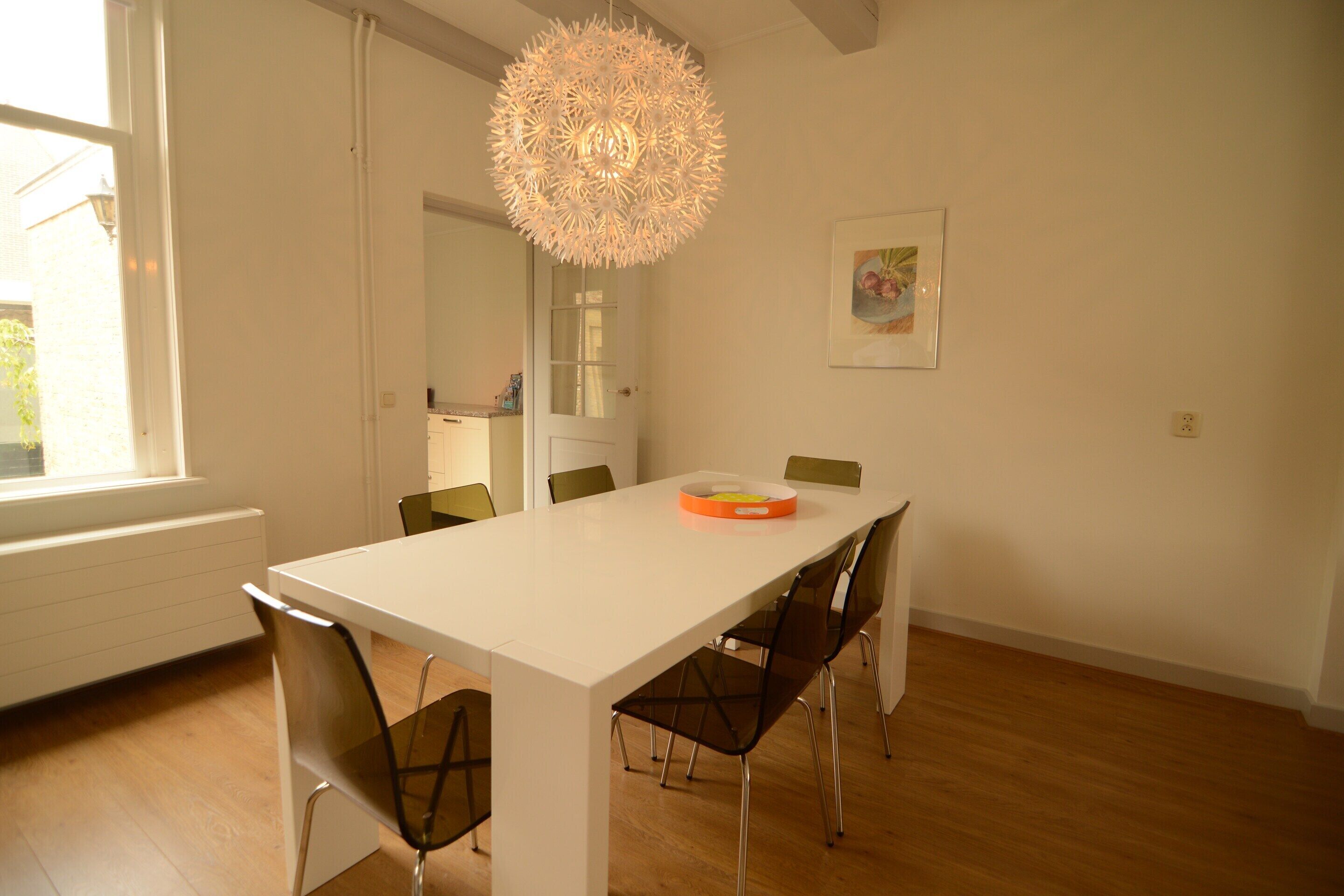 A dining area with a white table, four chairs, and a hanging light fixture.