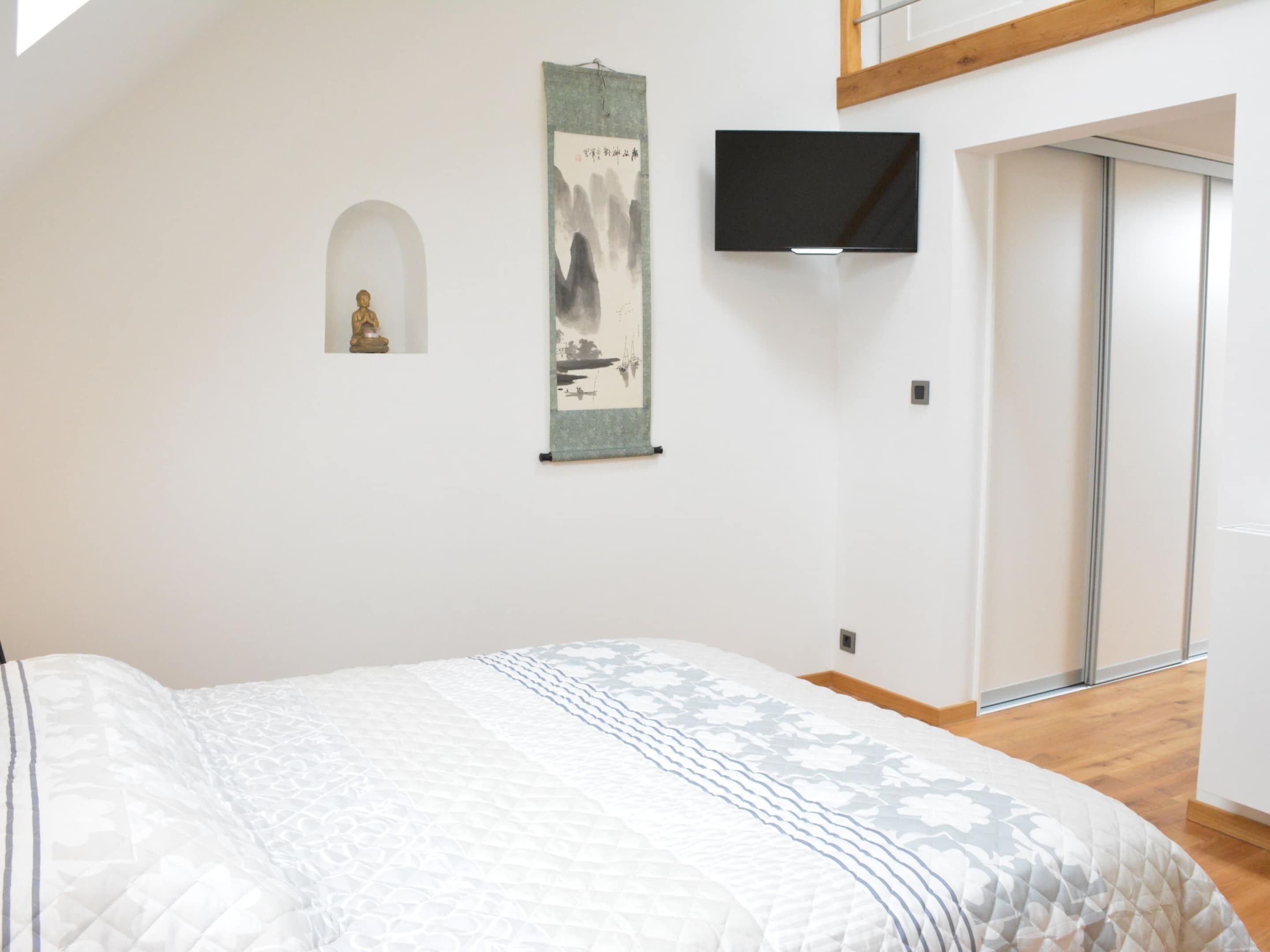 Une chambre à coucher avec un lit, un téléviseur fixé au mur, une petite statue et un tableau.