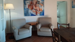 A living room with two armchairs, a small round table, and a dining table with chairs. There is a floor lamp and a painting on the wall. - Tuscan Hilltop Getaway (Castelnuovo di Val di Cecina)