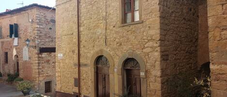 Ein Steinhaus mit Rundbogenportalen und einer Bank vor der Fassade.
